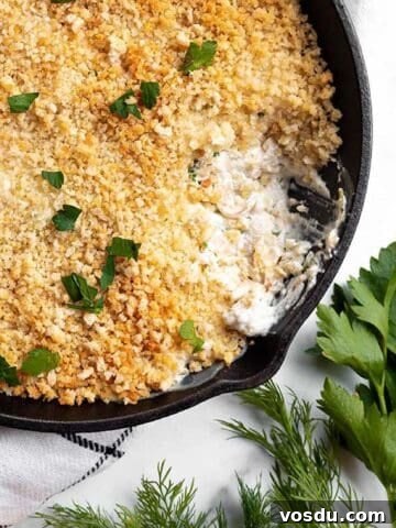 A small cast iron pan with a clam dip, panko top and some fresh herbs.