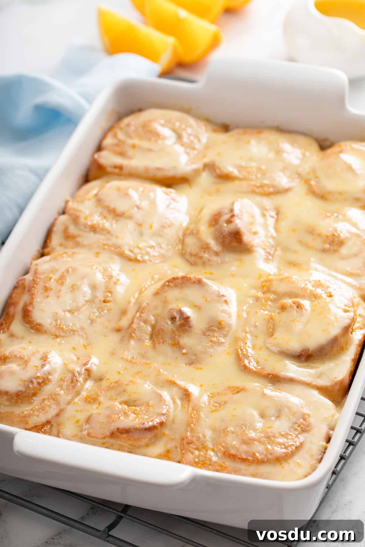 White baking dish filled with baked and glazed orange rolls.
