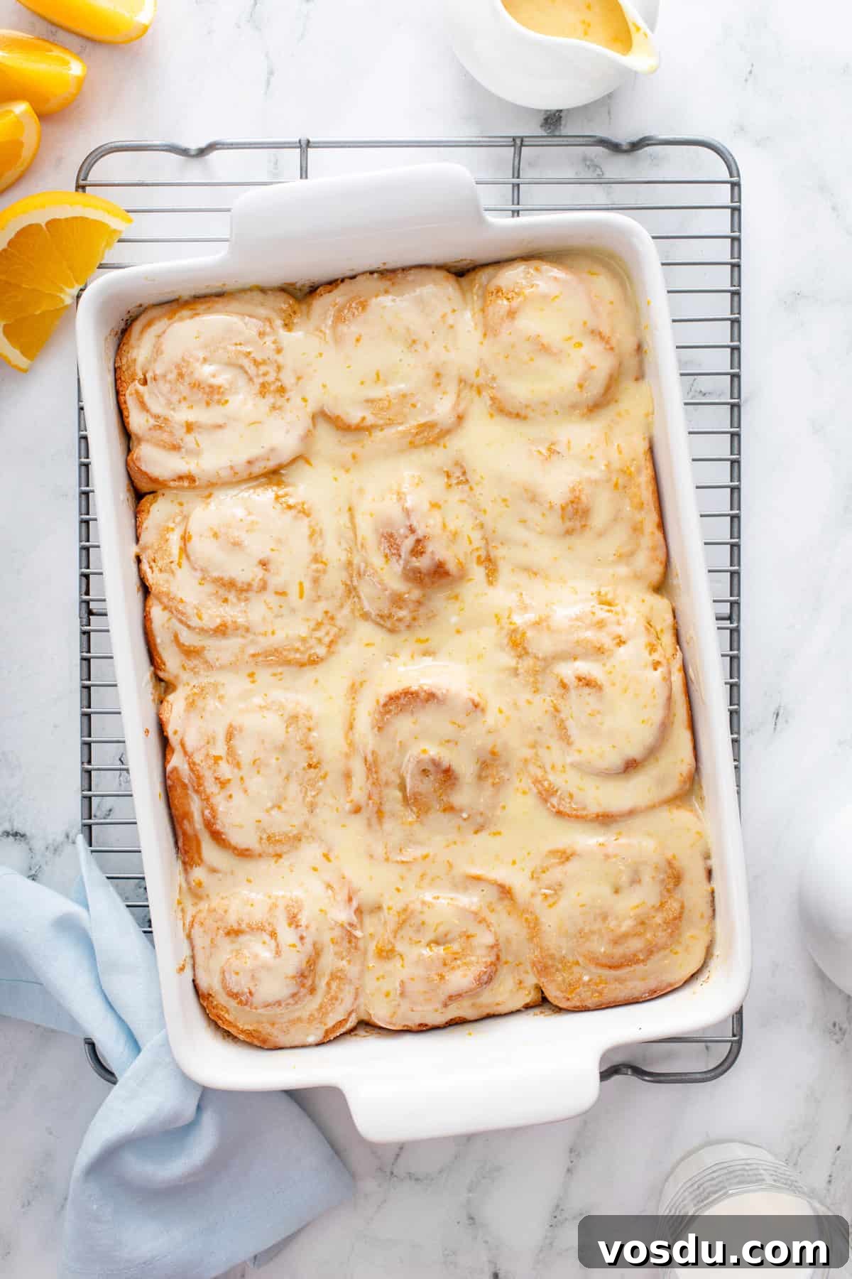 Overhead view of glazed sticky orange rolls in a white baking dish, set on a wire cooling rack.