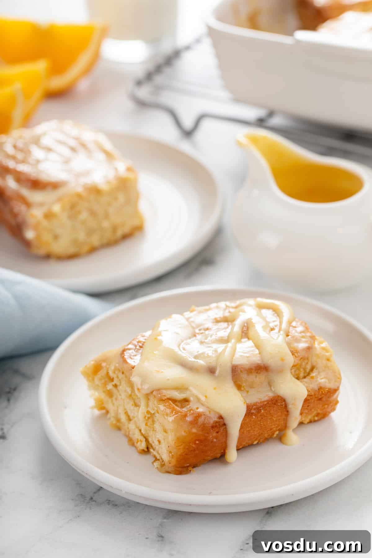 Two white plates holding sticky orange rolls, with a small pitcher of orange glaze in the background.