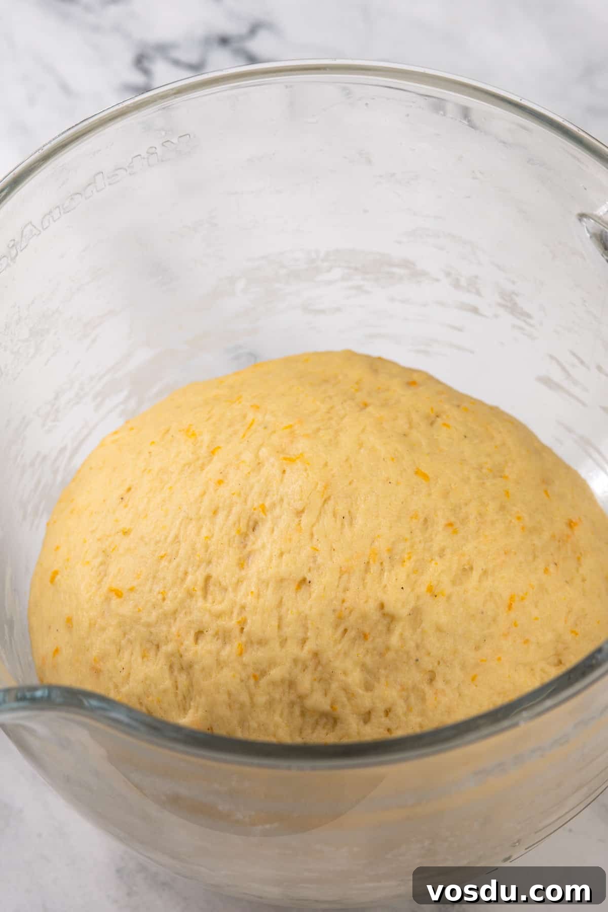 Risen orange roll dough in a glass bowl.