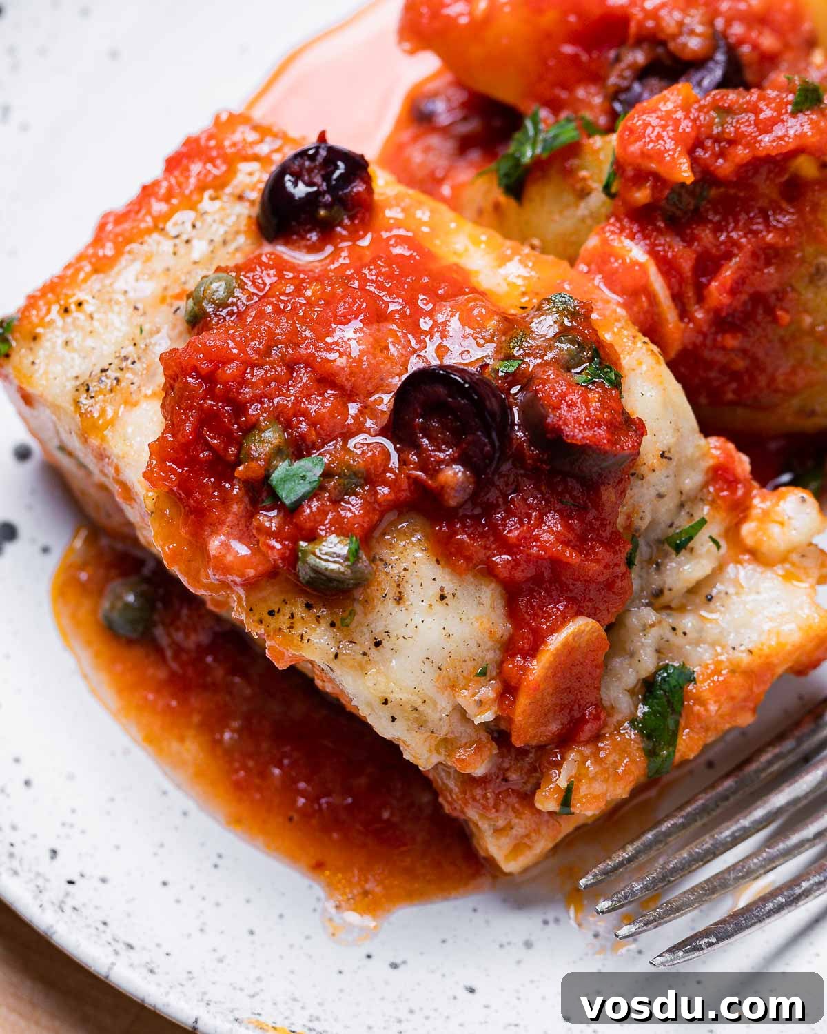 Neapolitan-Style Baccalà: Classic Salted Cod Recipe from Naples 10 Piece of baccala alla Napoletana in white plate with olives and capers on top.