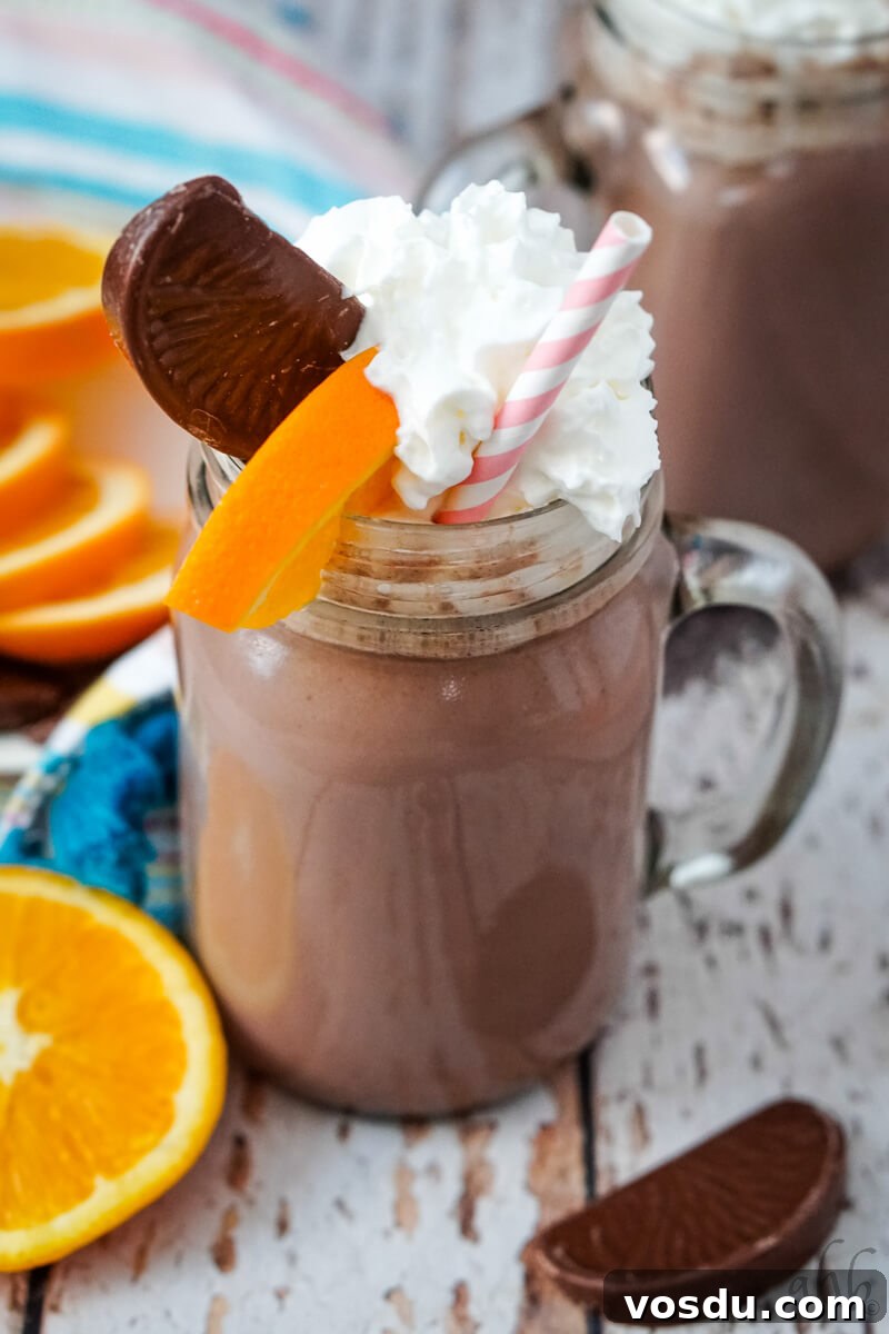 Velvety Orange Hot Chocolate Recipe: Creamy Spiced Cocoa 2 A mug of Orange Hot Chocolate garnished with whipped cream, a slice of Terry's chocolate orange, and a slice of orange.