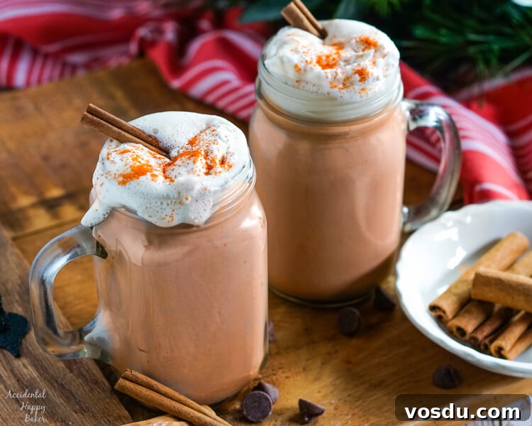 Velvety Orange Hot Chocolate Recipe: Creamy Spiced Cocoa 3 Clear glass mugs of Mexican Hot Cocoa topped with whipped cream and cinnamon sticks on a wooden tray.