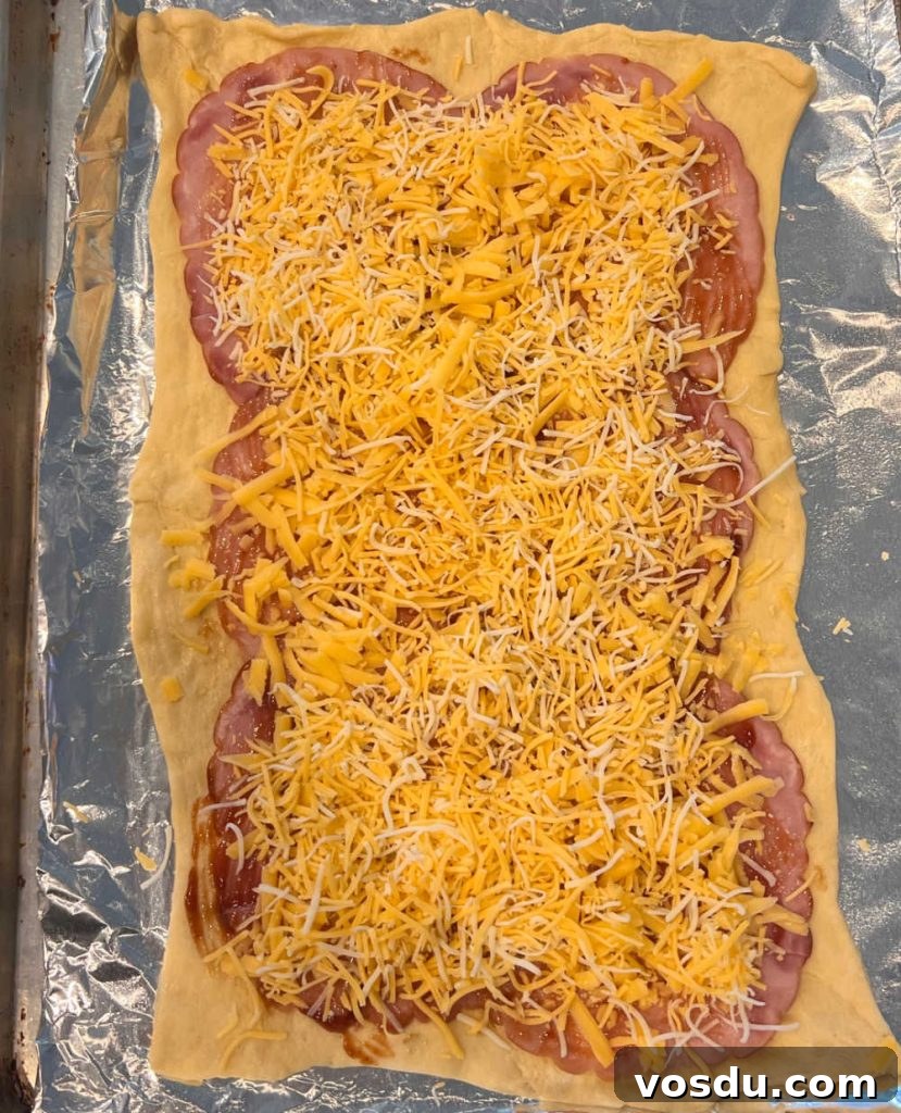 Ham and Cheese Crescent Roll-Ups Baked to Golden Perfection 5 crescent dough sheet topped with ham slices and shredded cheese on baking sheet