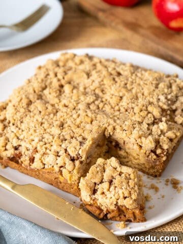 Applesauce crumb cake with a slice taken out on a white plate.