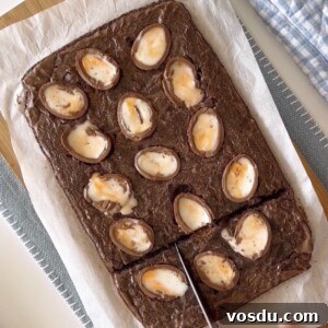 Slicing with a knife baked cadbury egg brownies on a wood cutting board.