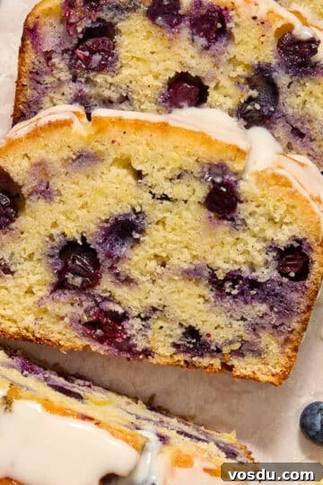 Slices of almond flour lemon blueberry bread topped with glaze and arranged on white parchment paper.