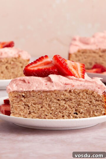 Side view of a slice of almond flour strawberry cake on a white plate with pieces of cake in the background.
