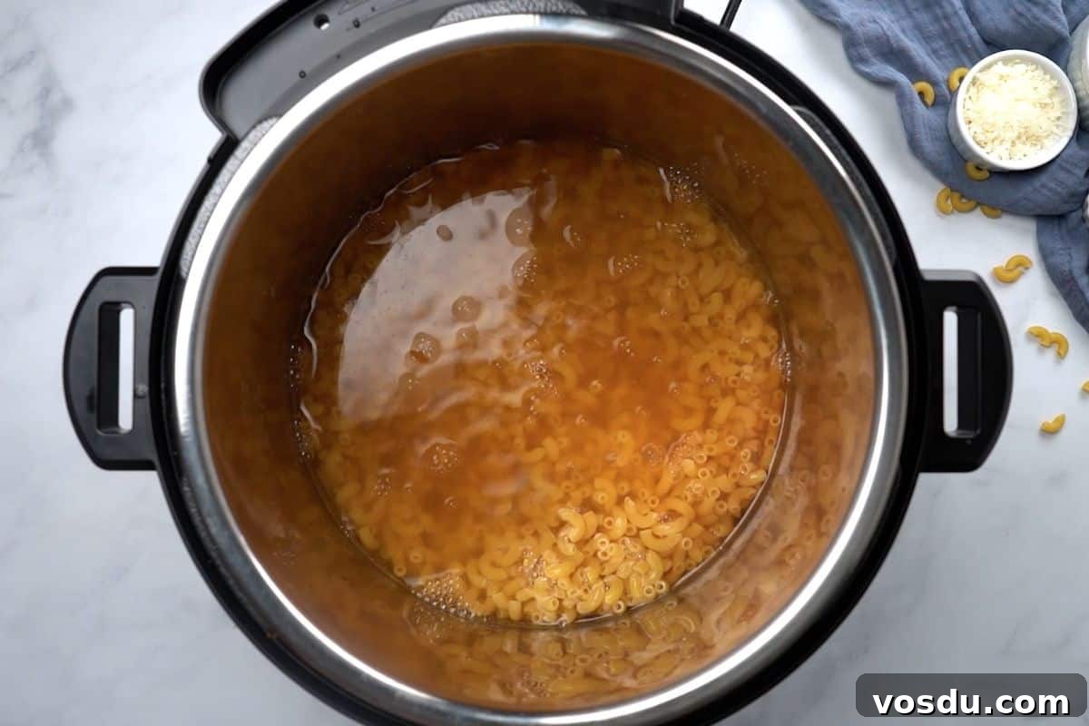 Recipe for Instant Pot Macaroni and Cheese Elbow noodles submerged in seasoned broth insider inner pot for mac and cheese recipe.