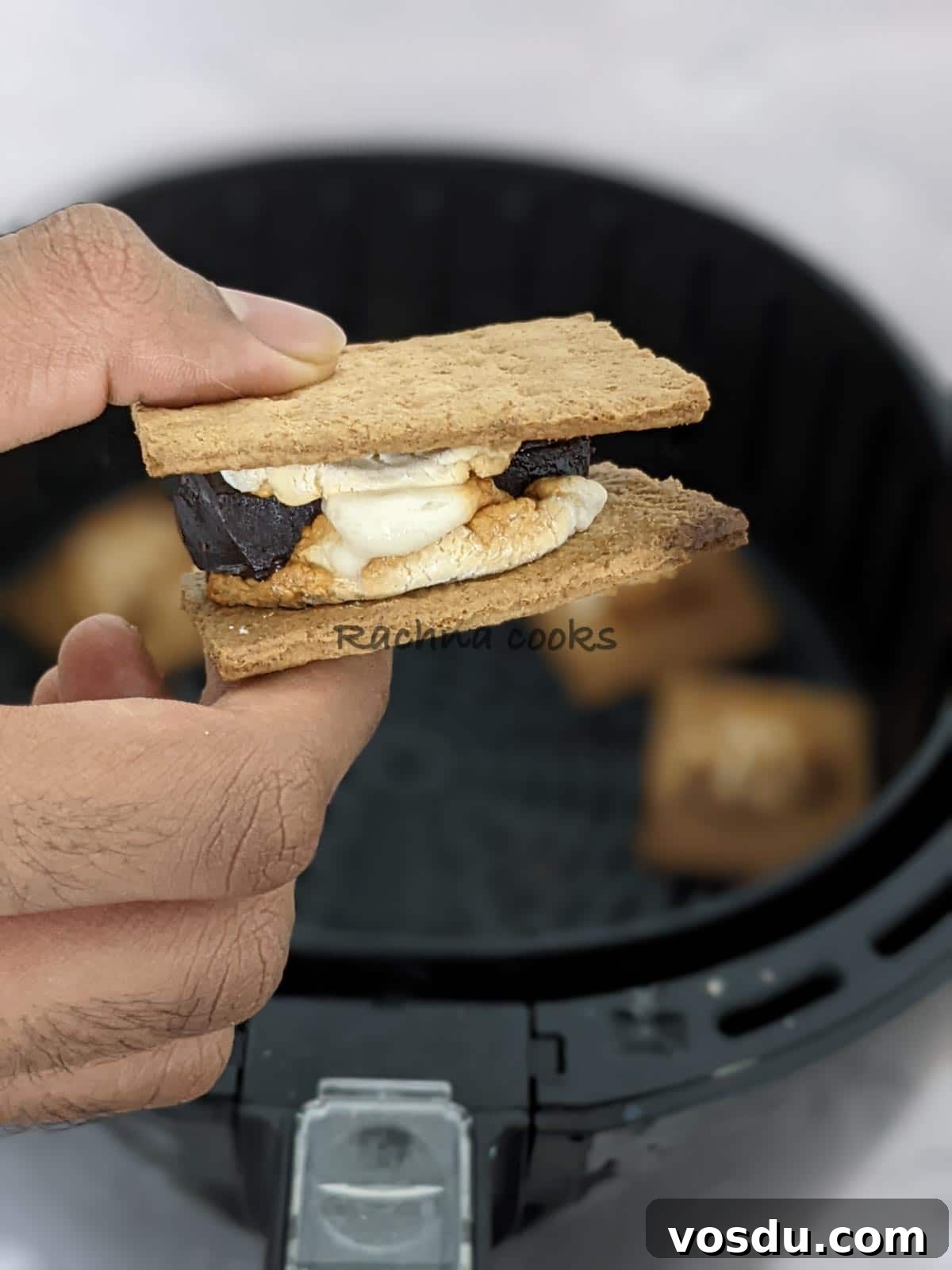 Crispy Air Fryer S'mores Recipe for Quick Desserts 2 One s'more held in hand with the background of air fryer basket.