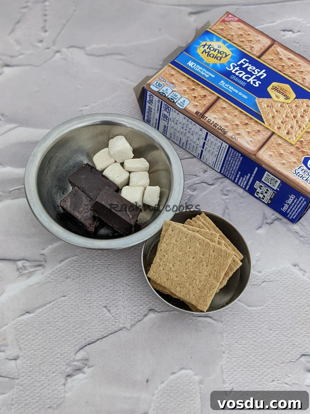 Crispy Air Fryer S'mores Recipe for Quick Desserts 3 Crackers in a bowl, marshmallows and chocolate bars in another bowl along with a pack of honey maid graham's crackers visible.