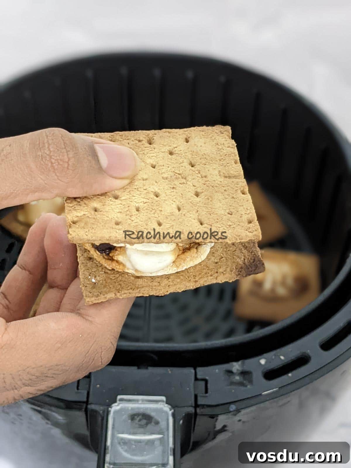 Crispy Air Fryer S'mores Recipe for Quick Desserts 4 One s'more held in hand with the background of air fryer basket.