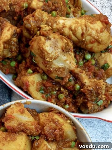 A dish of chicken bhuna made with chicken drumsticks, next to a side dish of Bombay potatoes.