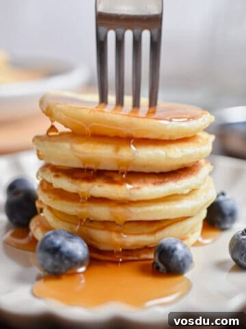 A fork is in a stack of silver dollar pancakes with maple syrup.