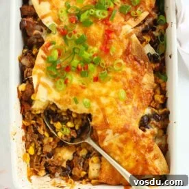 Looking down on a oven dish filled with Mexican beef with sweetcorn and beans, topped with tortillas and cheese, with a spoon dishing out.