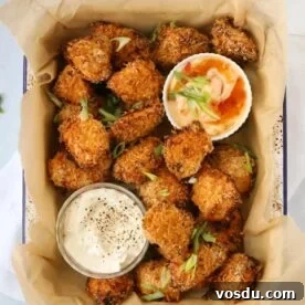 Coated golden homemade chicken nuggets in a baking dish with two pots of dips at the side.