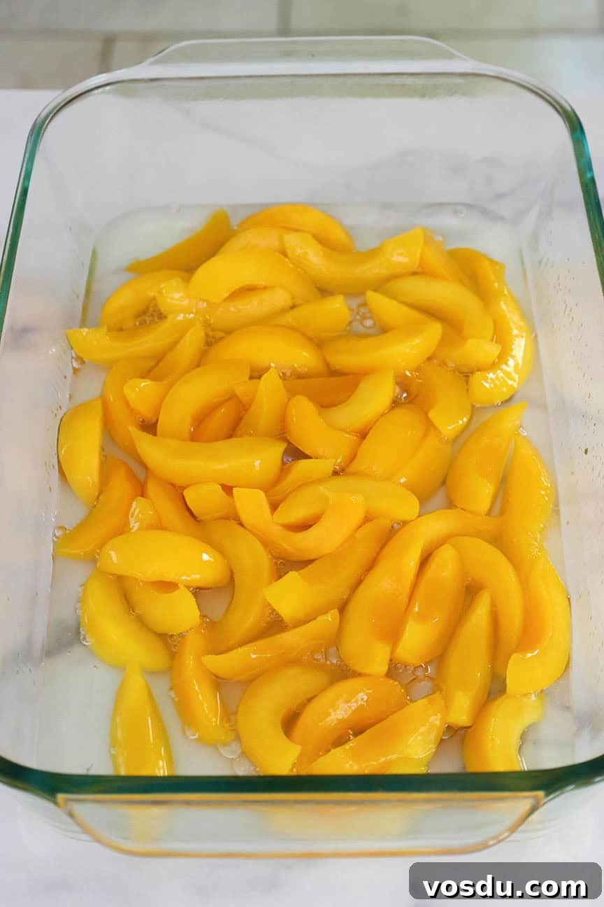 Quick Peach Cobbler Made with Cake Mix and Canned Peaches 4 A 9 by 13 inch glass baking dish with sliced peaches in syrup.