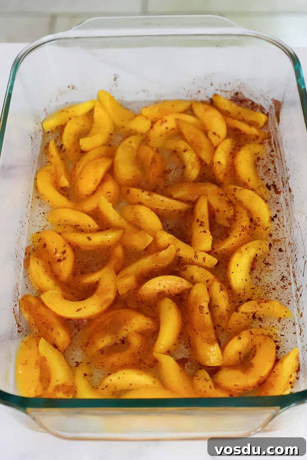Quick Peach Cobbler Made with Cake Mix and Canned Peaches 5 Sliced peaches in a baking dish sprinkled with cinnamon.