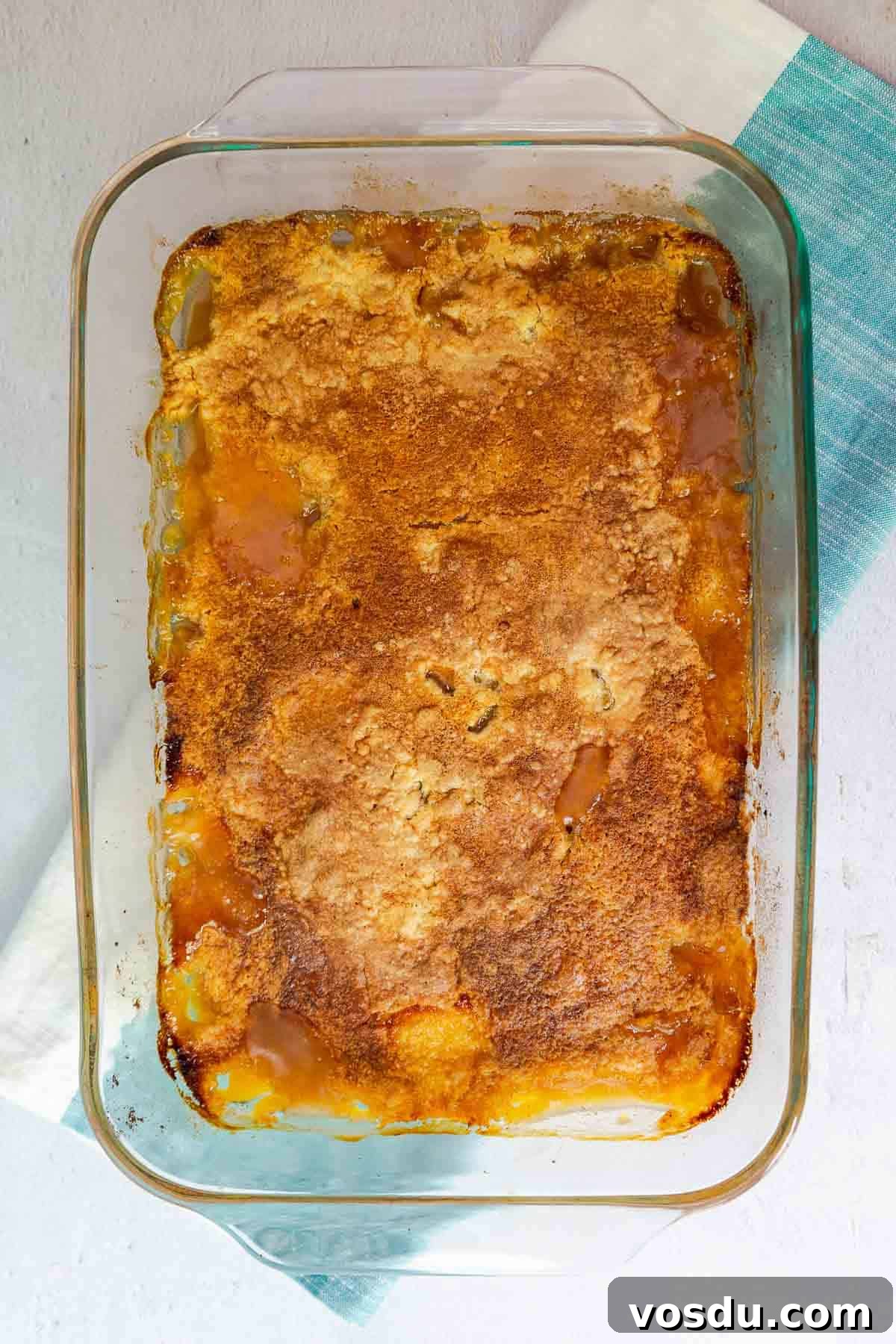 Quick Peach Cobbler Made with Cake Mix and Canned Peaches 8 A baked peach cobbler with a golden brown top in a glass dish.