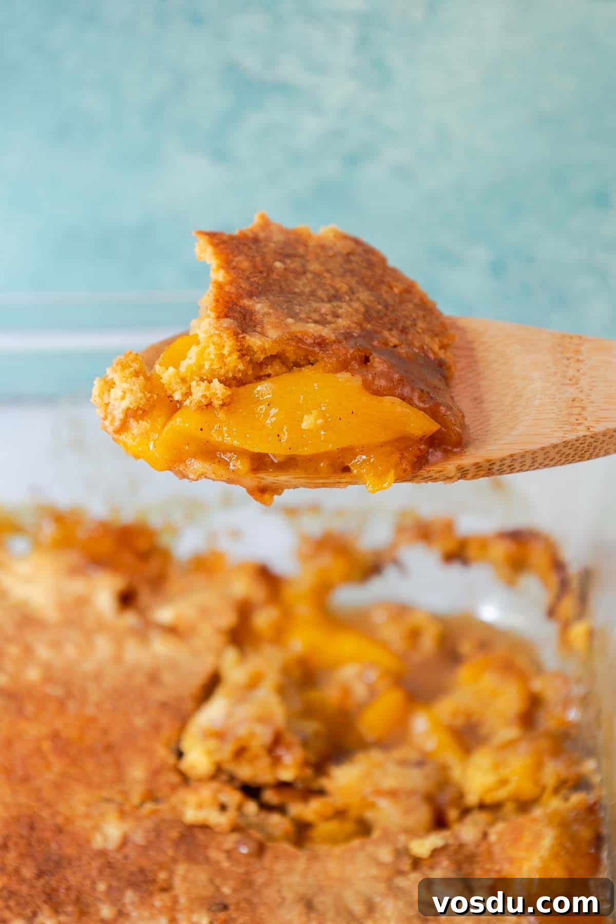 Quick Peach Cobbler Made with Cake Mix and Canned Peaches 10 A wooden spoon holding a scoop of peach cobbler.