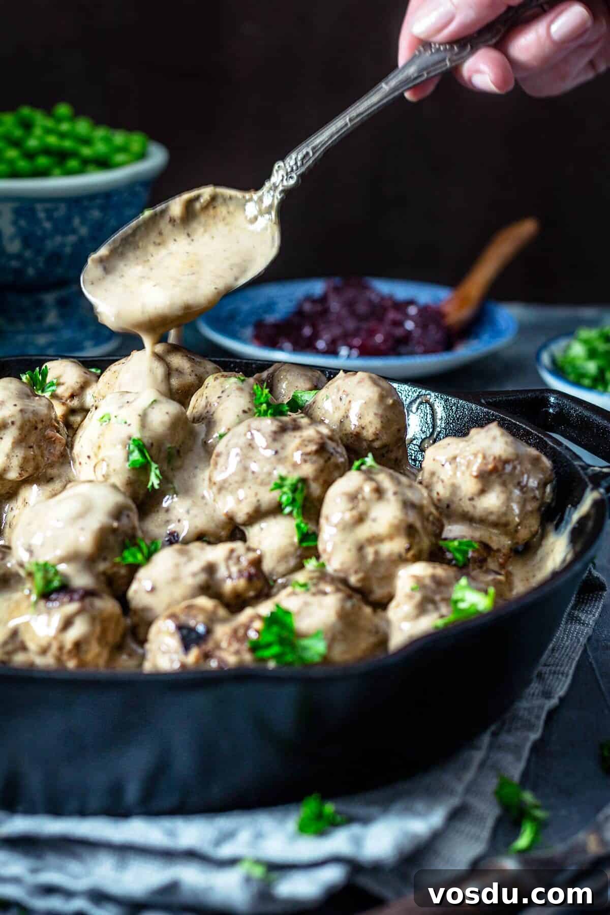 A person spooning gravy over the meatballs.