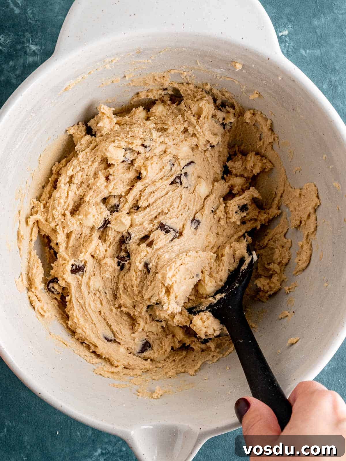 Folding dry ingredients and chocolate chips into wet cookie dough ingredients.