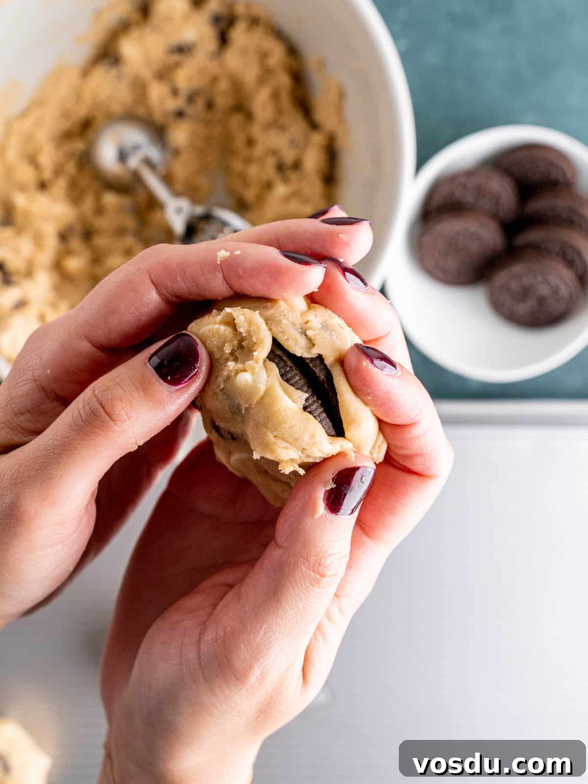 Hands covering an Oreo in chocolate chip cookie dough.