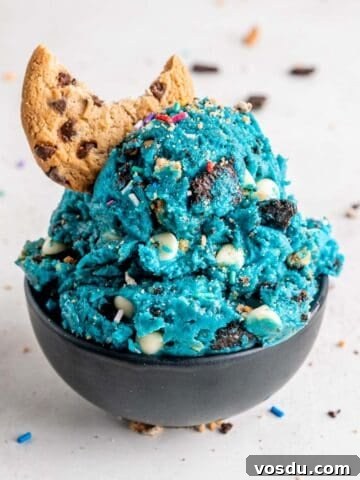 Scoops of edible cookie monster cookie dough with a chocolate chip cookie in a bowl.
