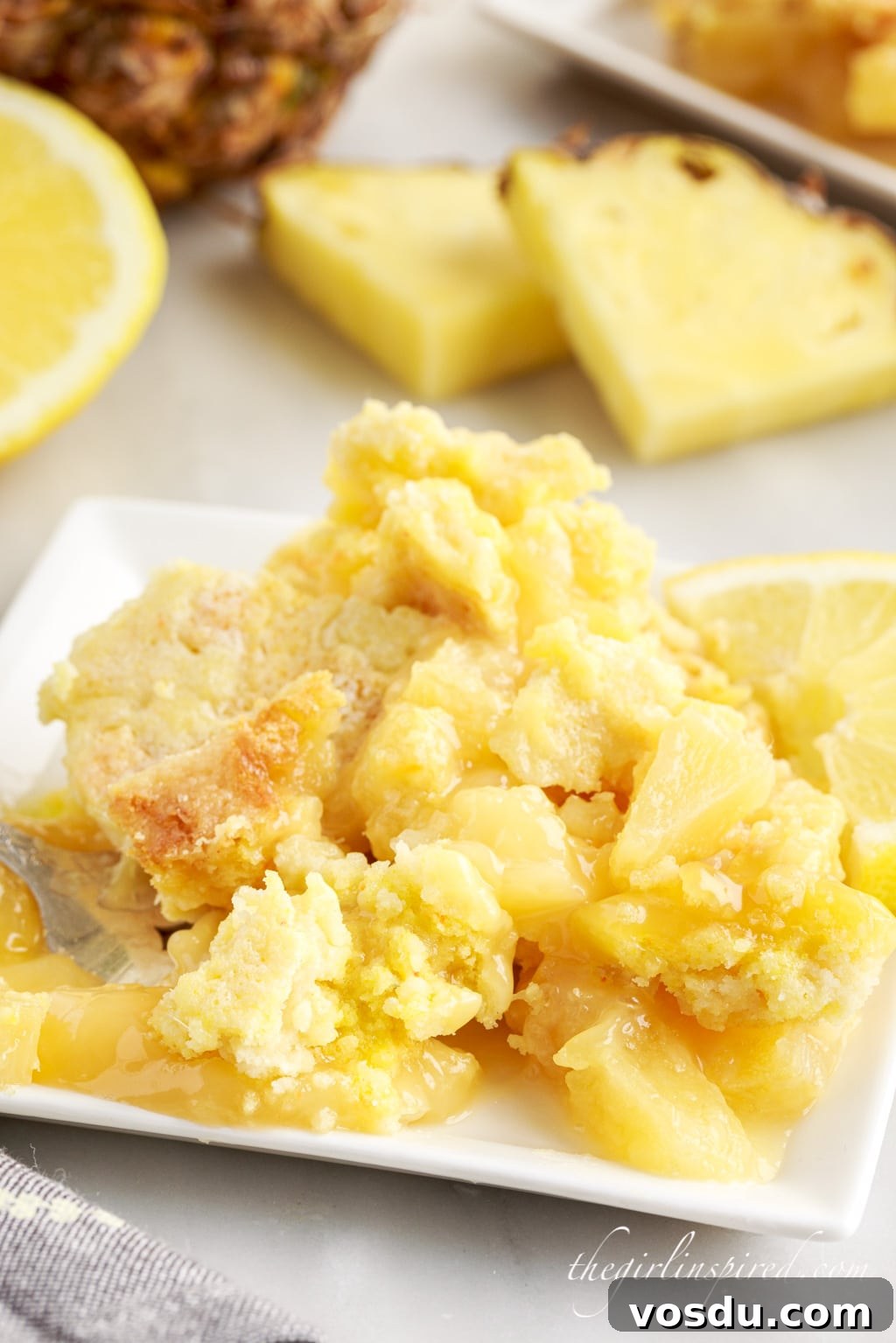 Tangy Lemon Pineapple Dump Cake Recipe for Summer Dessert 2 Lemon dump cake on a plate with pineapple in the background.