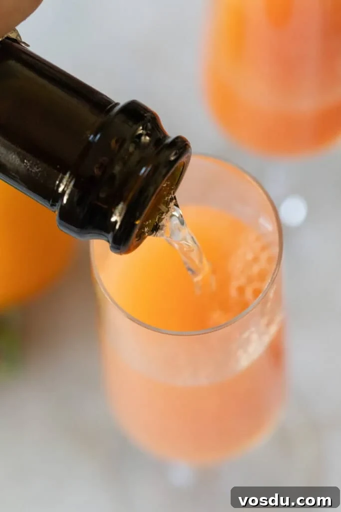 Citrus Grapefruit Mimosa Recipe — Bright Brunch Cocktail 5 Pouring Champagne into a Champagne glass to make a grapefruit mimosa.