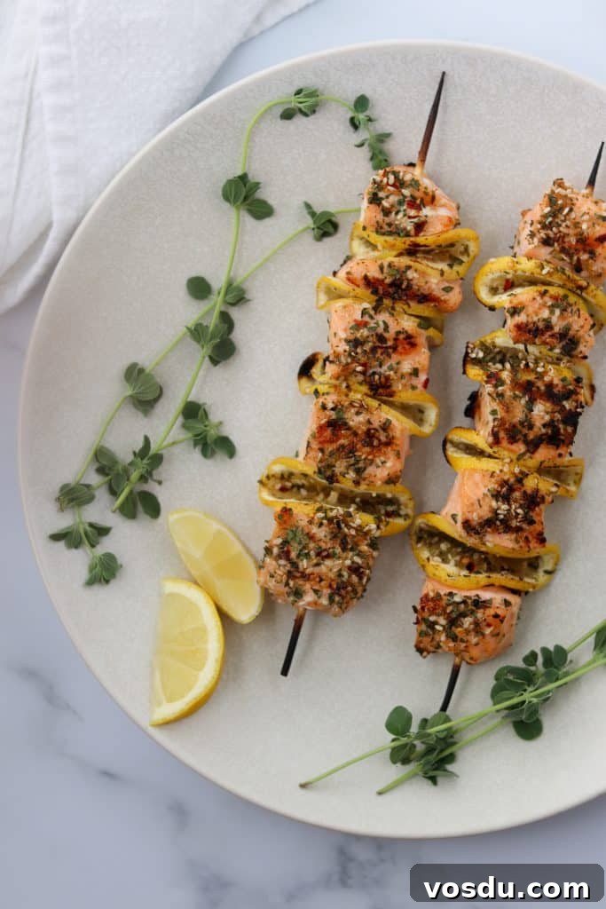 Lemon-Spiced Salmon Skewers with Herb Marinade 2 Salmon skewers on a plate with lemon wedges and fresh herbs