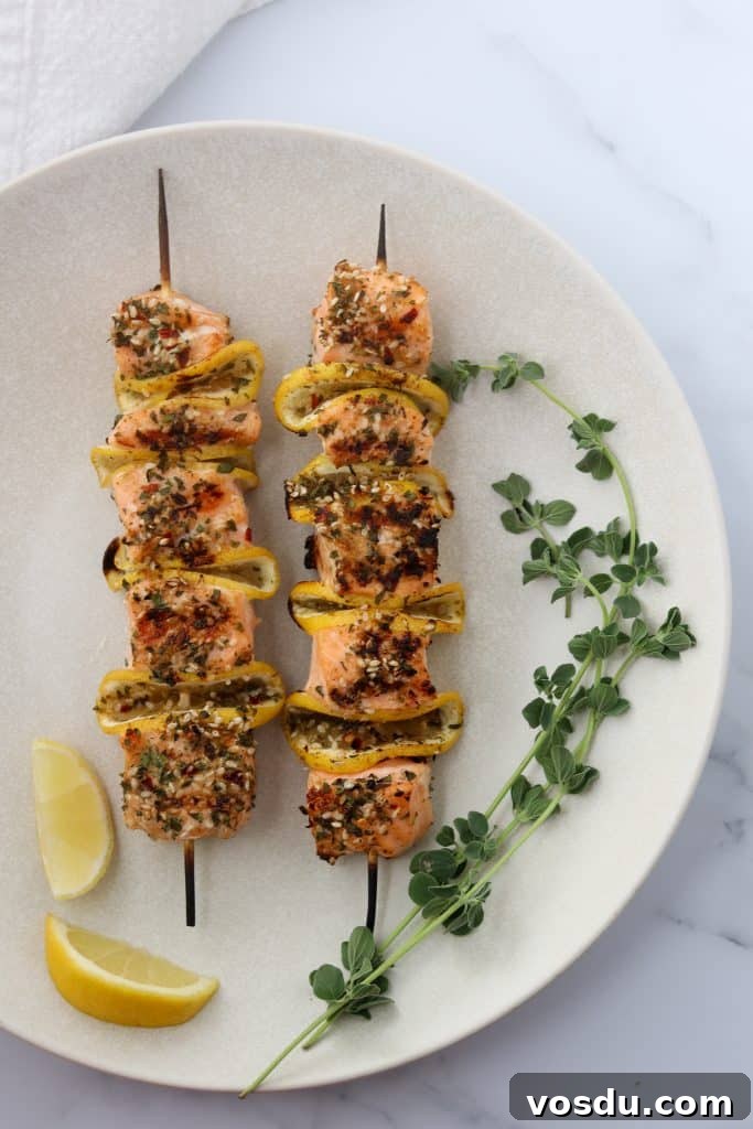 Lemon-Spiced Salmon Skewers with Herb Marinade 6 Salmon skewers on a plate with fresh herbs and lemon wedges