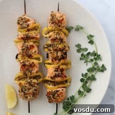 Lemon-Spiced Salmon Skewers with Herb Marinade 7 Salmon skewers on a plate with fresh herbs and lemon wedges