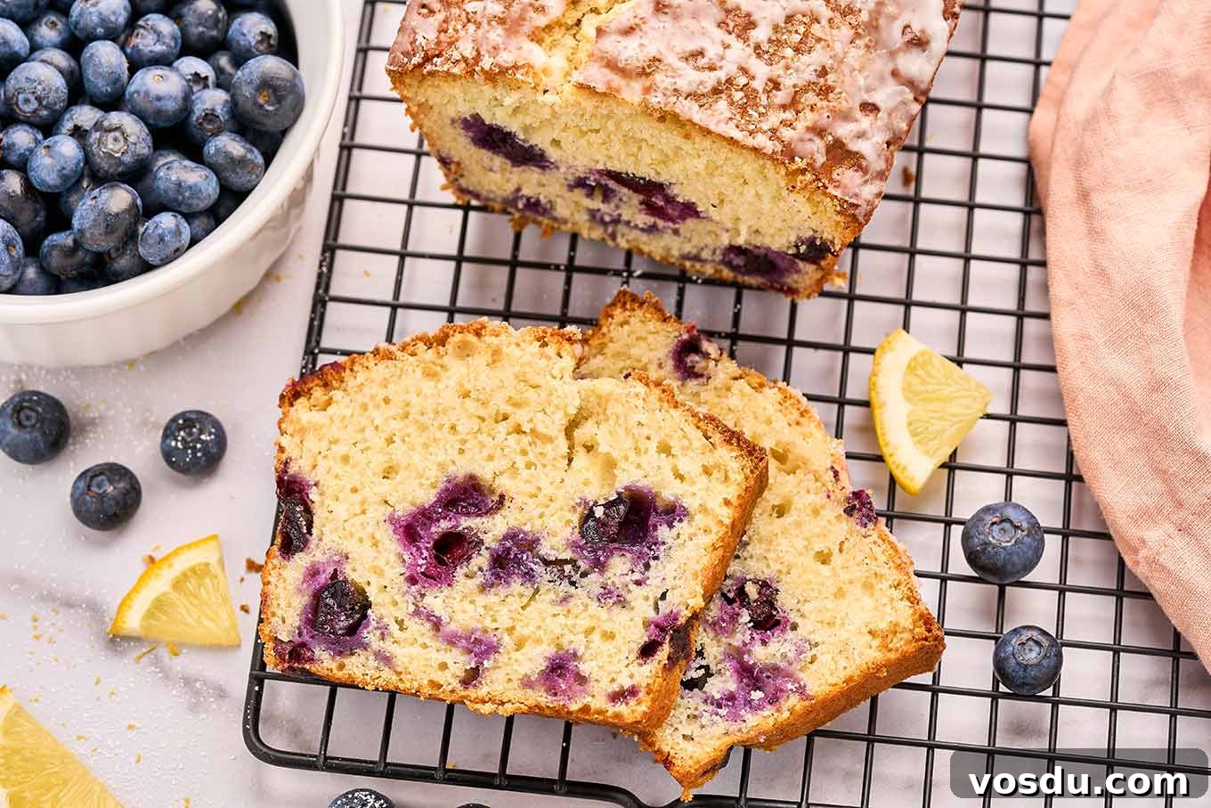 Lemon Blueberry Loaf Cake Recipe with Zesty Glaze 4 Close-up of a sliced lemon blueberry loaf cake on a cooling rack showing juicy blueberries throughout the moist crumb.