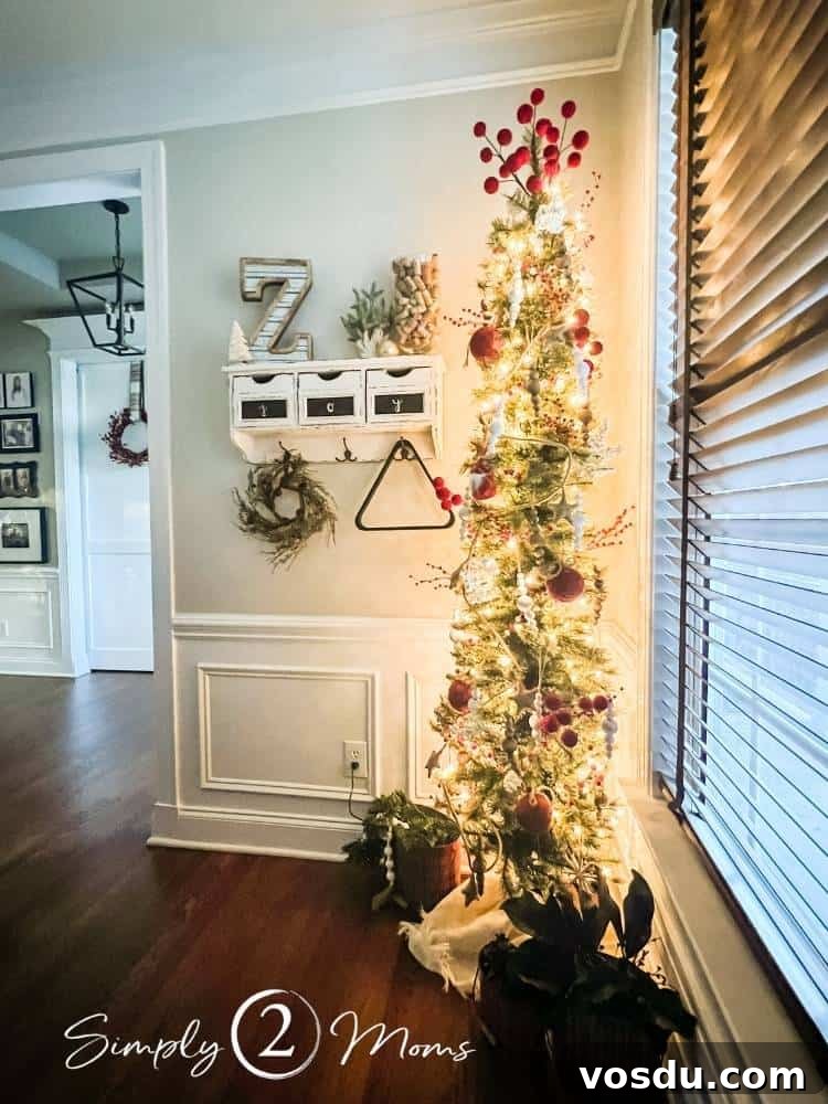 Country Chic Christmas Home Tour That Inspires Holiday Decorating 13 Slim Christmas tree with red and white decorations in a game room next to a wall shelf with hooks and a small wreath. View into a foyer with a gallery wall.