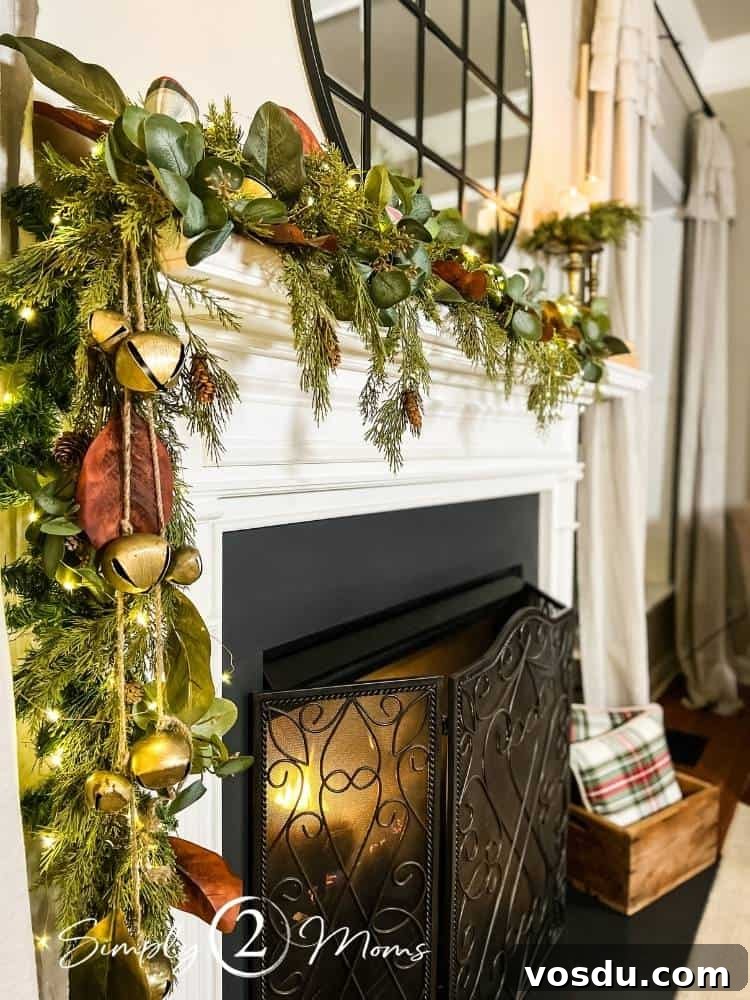 Country Chic Christmas Home Tour That Inspires Holiday Decorating 17 Close up view of a gas fireplace decorated for Christmas with asymmetrical garland and gold sleigh bells.