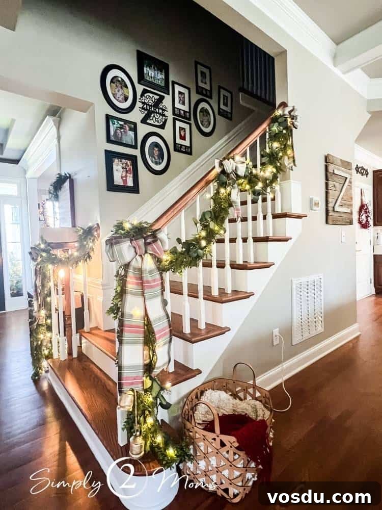 Country Chic Christmas Home Tour That Inspires Holiday Decorating 18 Wood staircase with painted risers decorated for Christmas with greenery garland wrapped in twinkle lights held by large plaid bows. A gallery wall with black frames goes up the stairway wall.