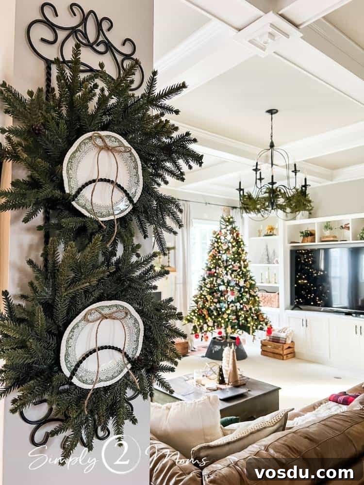Country Chic Christmas Home Tour That Inspires Holiday Decorating 19 Iron scrollwork plate rack with wreaths and small green Wedgewood plates on a wall next to a family room with classic iron chandelier and Christmas tree.