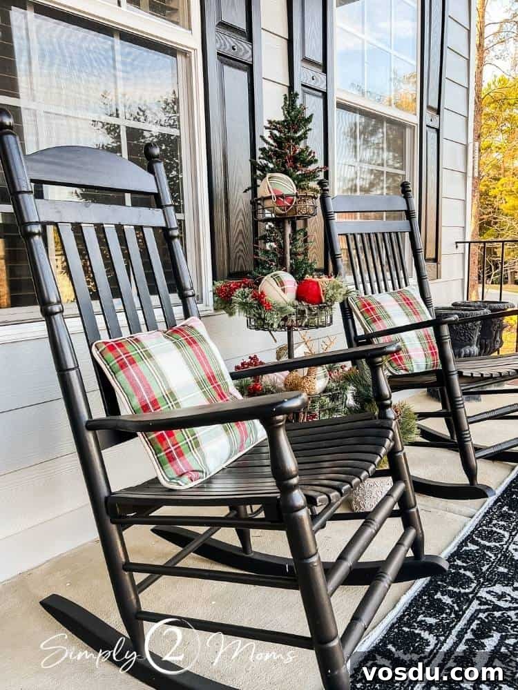 Country Chic Christmas Home Tour That Inspires Holiday Decorating 3 Two black rocking chairs on a front porch with Christmas plaid throw pillows and a tiered stand decorated for Christmas between them.