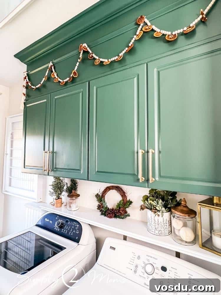 Country Chic Christmas Home Tour That Inspires Holiday Decorating 27 Green painted laminate cabinets in a laundry room decorated for Christmas with a dried orange garland hanging above the cabinets.
