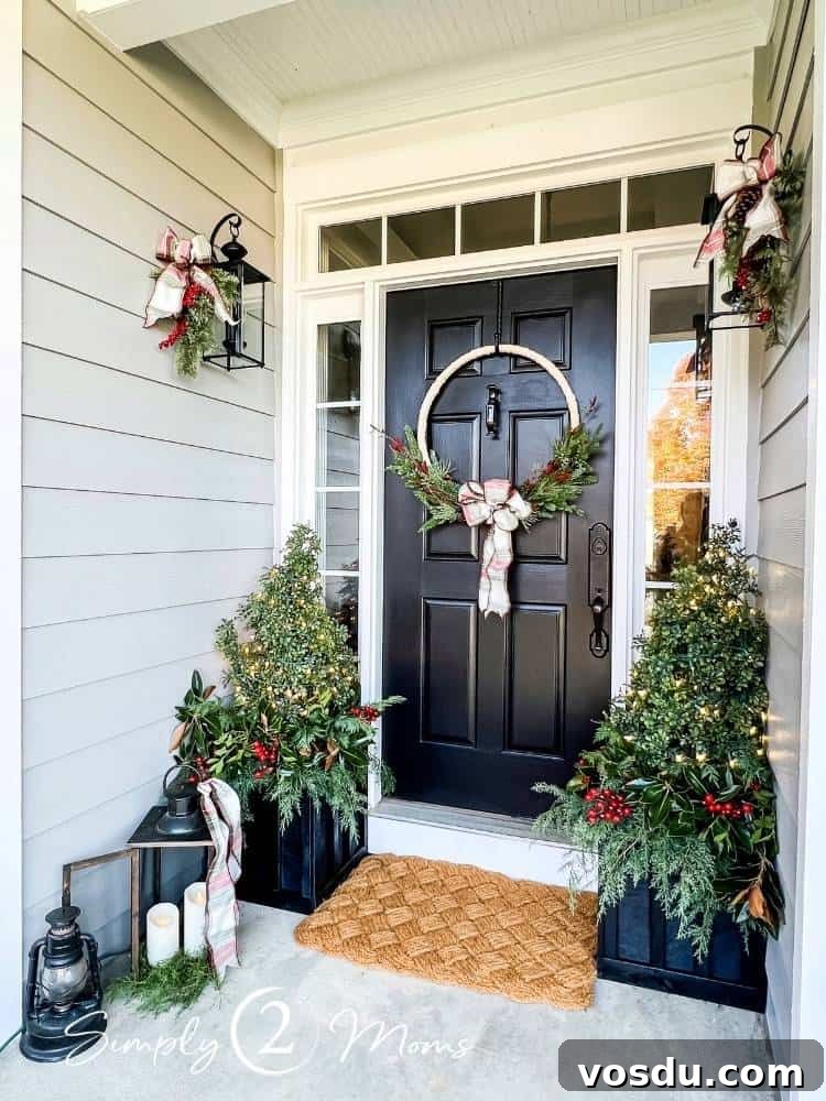 Country Chic Christmas Home Tour That Inspires Holiday Decorating 4 Black front door with a large hoop wreath and transom and side lights decorated for Christmas. Two black square planter boxes on each side of the door filled with greenery and faux topiary with lights.