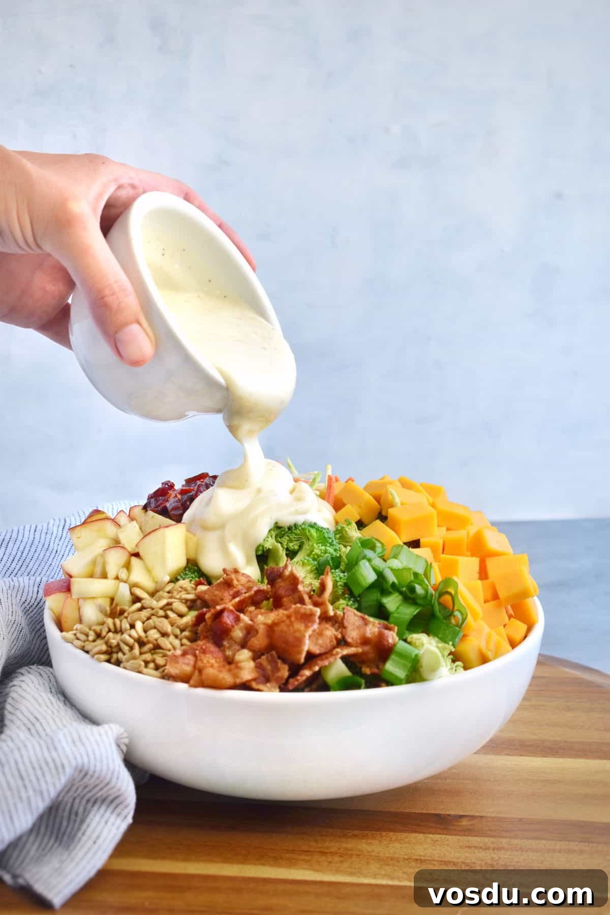 Broccoli Salad with Greek Yogurt Dressing – Light and Creamy 6 dressing being poured over top of salad in bowl.