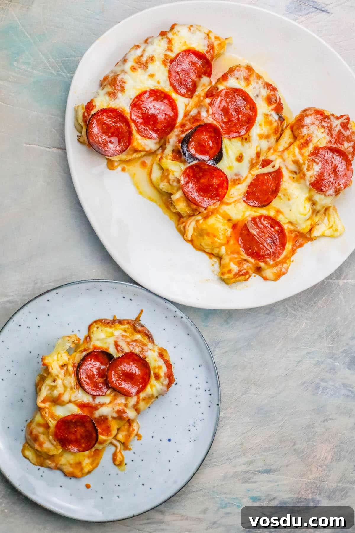 Keto Low-Carb Cheesy Pizza Chicken Recipe 2 chicken smothered in cheese and pepperonis on a plate