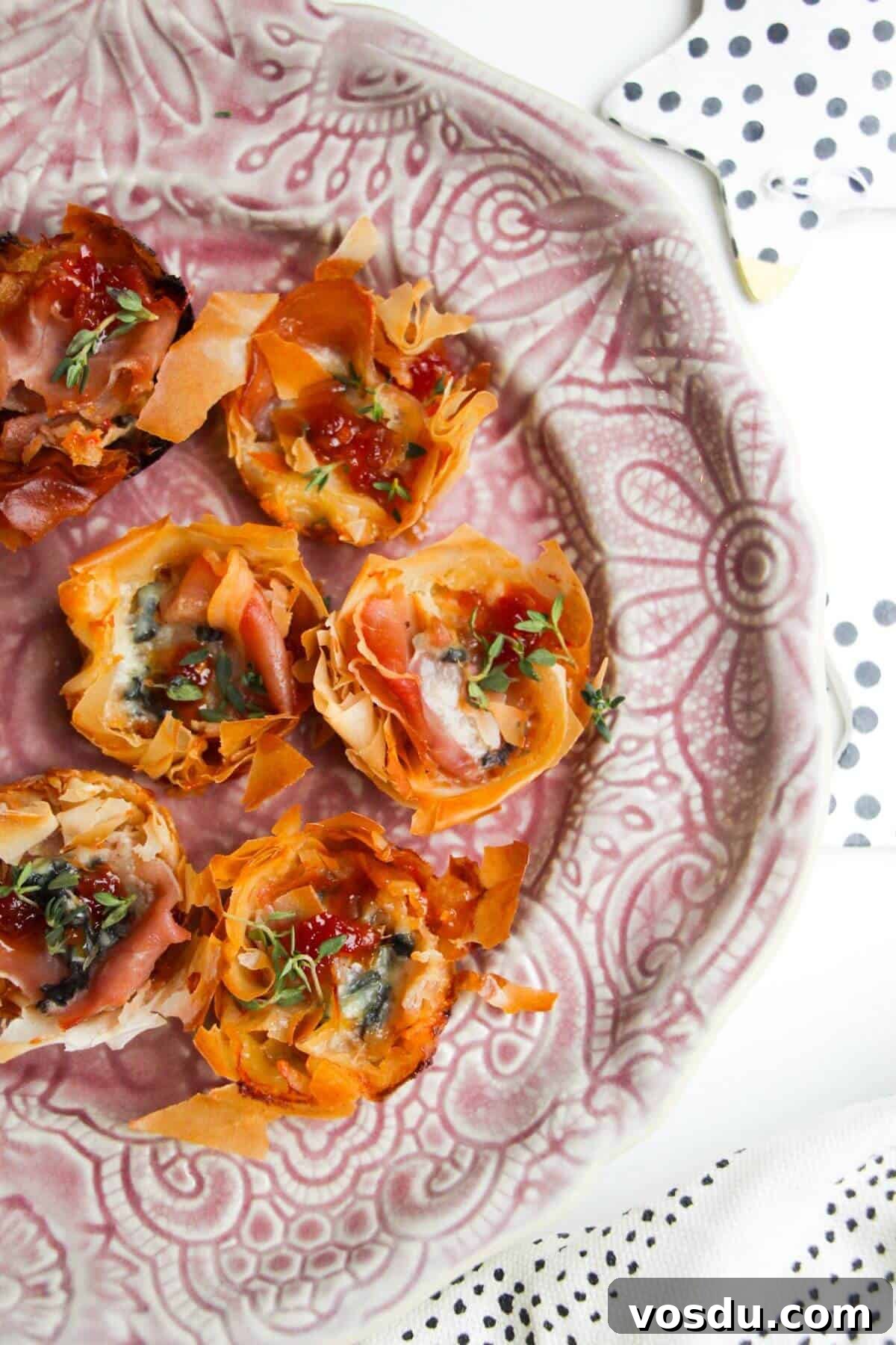 Blue Cheese, Prosciutto & Sweet Chili Filo Cups Recipe 2 Baked blue cheese, prosciutto, sweet chilli bites on a small pink plate.