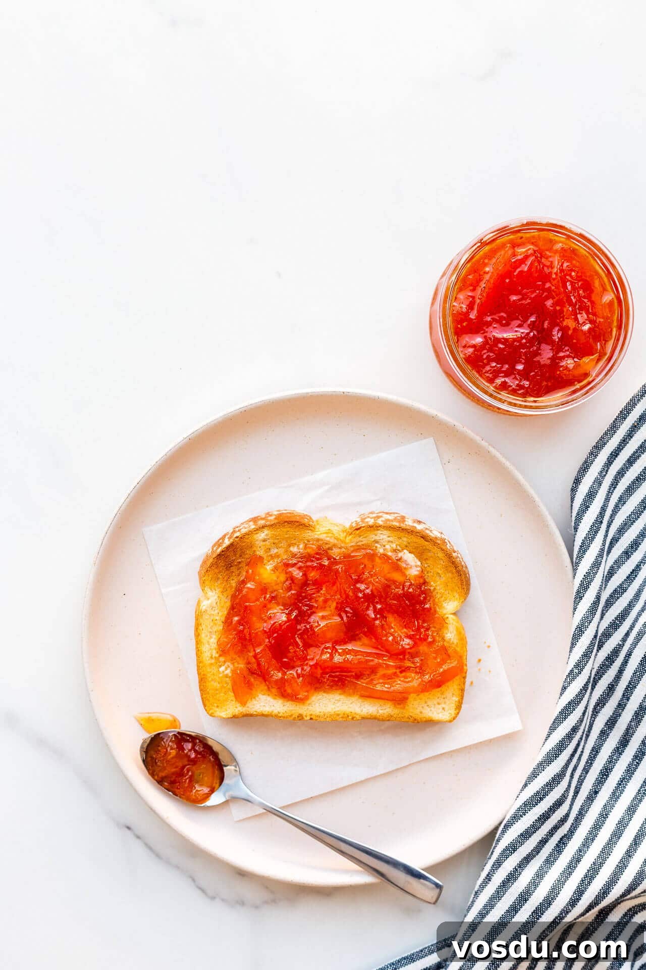 Pink grapefruit marmalade on toast on a plate with a striped linen.