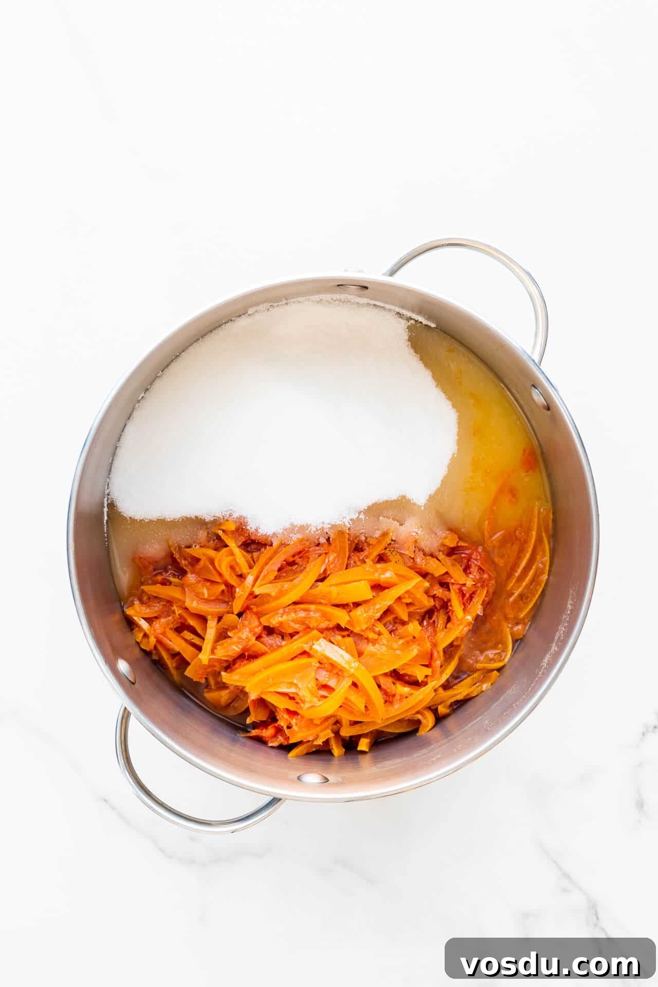 A stainless steel pot with sliced citrus fruit, sugar, and lemon juice, ready to make marmalade.
