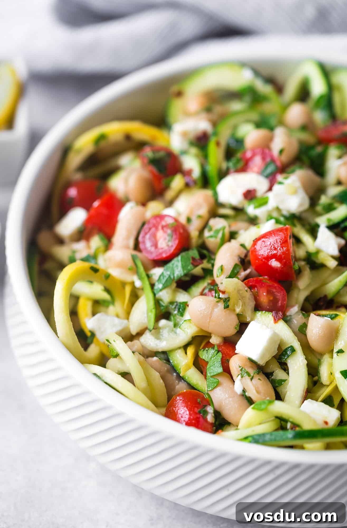 Zucchini Noodle Salad with White Beans, Feta & Lemon Vinaigrette 2 Zucchini noodles in a white bowl with fresh herbs, tomatoes, black beans.