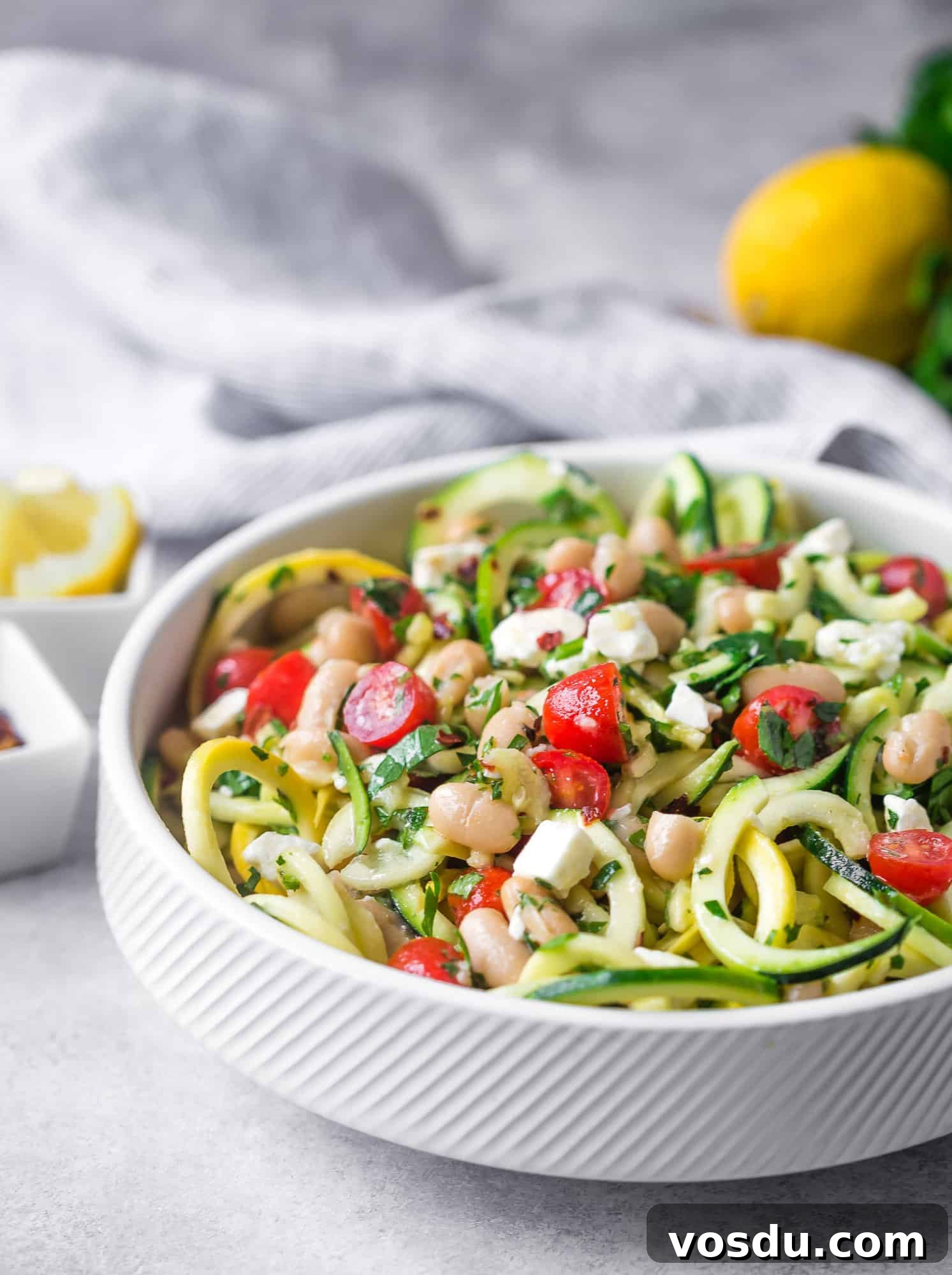 Zucchini Noodle Salad with White Beans, Feta & Lemon Vinaigrette 3 Zucchini noodle salad in a white bowl with tomatoes, feta, beans.