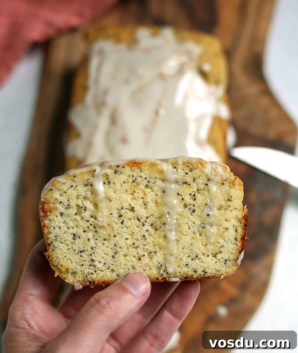 A hand holding a slice of lemon poppy seed bread with glaze dripping down.
